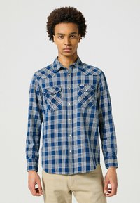 Camisa de cuadros en azul marino y blanca de manga larga con dos bolsillos en el pecho, cuello abotonado y dobladillo curvo. Fabricada en tejido tejido.