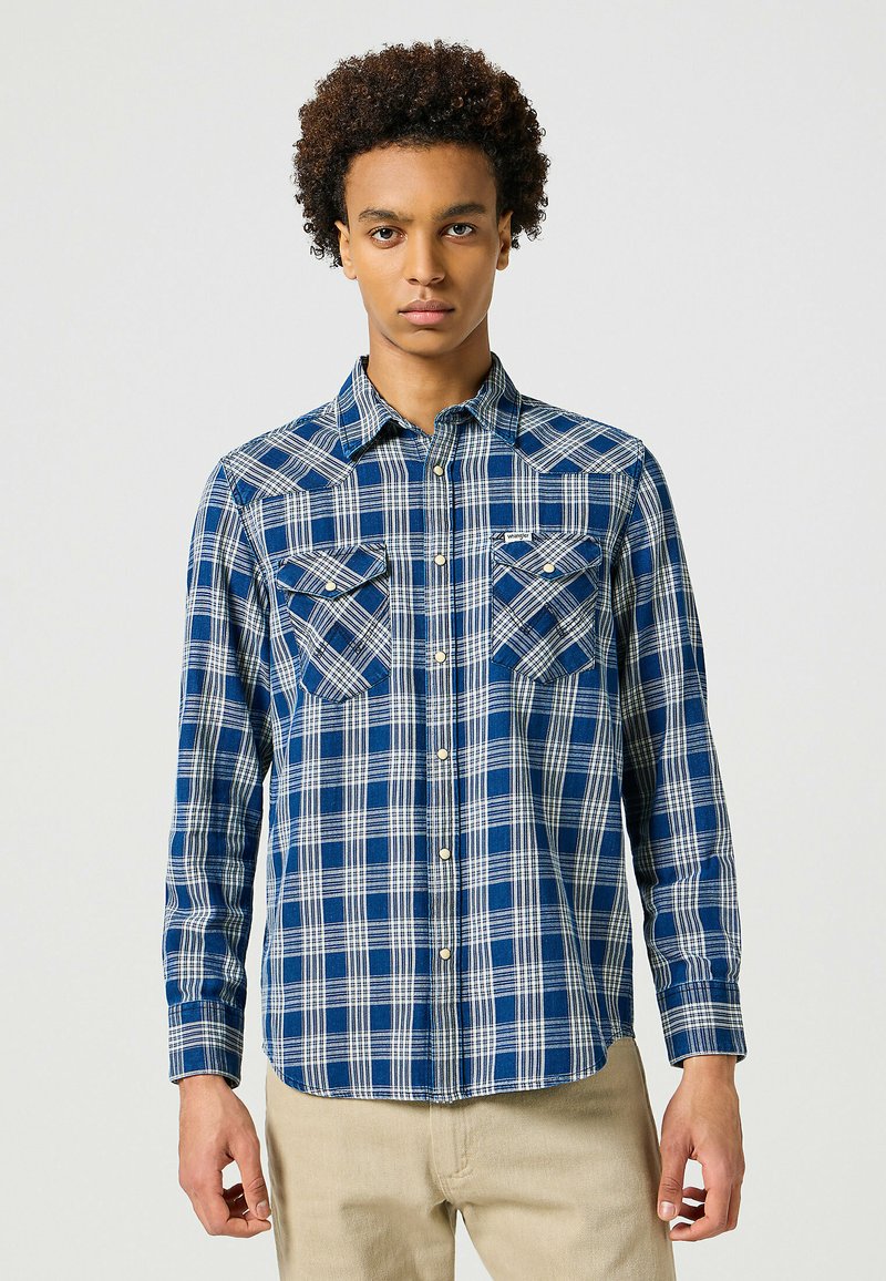Camisa de cuadros en azul marino y blanca de manga larga con dos bolsillos en el pecho, cuello abotonado y dobladillo curvo. Fabricada en tejido tejido.