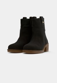 Bottines en daim noir avec un bout arrondi et un petit talon empilé. Comprend une couture sur le devant et des languettes sur les côtés pour un enfilage facile.
