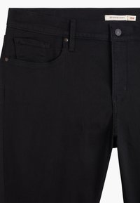 Sorte denim jeans med smal passform, med en frontlomme, knappestenger og stikninger. Merket viser modellnummer 311 og størrelse 18W.