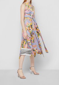 Robe bleu clair à motifs floraux avec ceinture à nouer, associée à un sac à main métallique argenté et des talons argentés à brides.