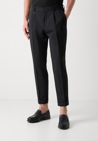 Pantaloni negri, croiți, cu un finisaj neted, având un bragulet confortabil, tiv cu manșetă și pliseuri laterale subtile. Purtați cu mocasini negri.