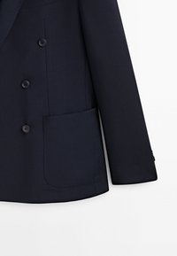 Blazer bleu marine foncé avec trois boutons, une grande poche plaquée et manches longues sur fond blanc.