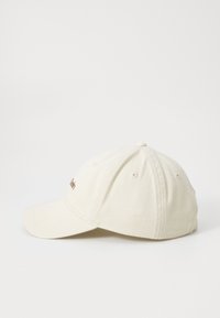 Baseball cap i lys beige stoff, med buet brem, justerbar stropp og subtil broderi på fronten. Teksturert finish.