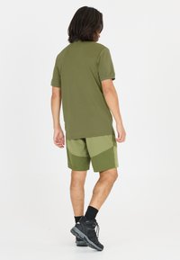 Herrskjorta med kort ärm och shorts i olika nyanser av olivgrön, tillverkade av lätt och ventilerande tyg; skjortan har en enkel, figurnära design.