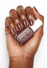 Vernis à ongles bordeaux foncé dans un flacon transparent avec un capuchon blanc. Les doigts montrent une finition brillante sur les ongles. Le texte sur le flacon indique "essie."