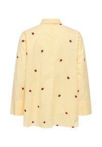Chemise jaune à manches longues avec broderie de fraises rouges dispersées dans le dos, dotée d'un col classique et de larges poignets.