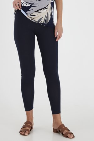 Navy leggings made of stretchy material, fitted design, ankle-length, paired with brown strappy sandals, worn with a patterned top.