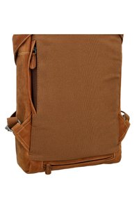 Rudas odinis ir kanvoso kuprinė su tekstūruota paviršiumi, turinti šoninio užtrauktuko kišenę ir reguliuojamą petnešą.