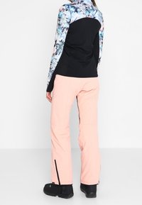 Maglietta a maniche lunghe nera con motivo floreale abbinata a pantaloni rosa chiaro; calzature nere con cerniere alle caviglie dei pantaloni.