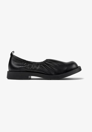 Zapato plano de cuero negro con un upper elástico y recogido, punta redondeada y tacón cuadrado bajo. Textura suave y diseño minimalista.