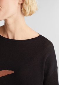 Svart tröja med rundad halsringning. Har ett ljusbrunt abstrakt mönster på framsidan. Mjuk textur, något genomskinligt tyg.