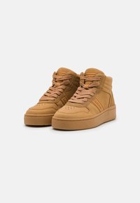 Hoge sneakers in tan suède met een gestructureerde bovenkant, platte veters, versterkte neus en gevoerde kraag. Glanzende rubberen zool voor grip.