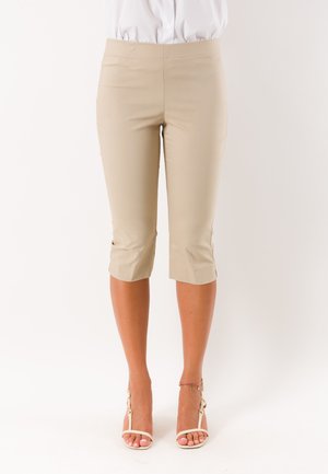 Pantaloni capri beige slim fit indossati con tacchi bianchi con cinturini e camicia bianca infilata.