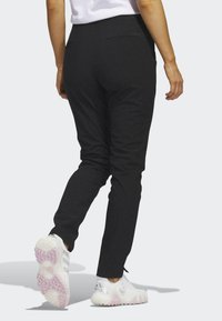 Calças pretas justas com uma textura suave, apresentando bolsos traseiros e um design elegante, combinadas com sapatilhas brancas com detalhes em rosa.