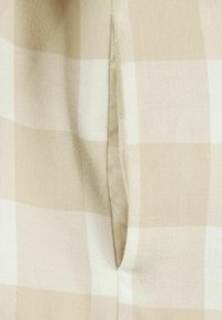 Tissu à carreaux beige et blanc avec une texture douce, présentant des carreaux distincts et un détail de couture visible au centre.