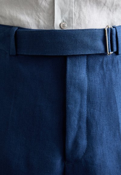 Pantalones de lino azul marino con una textura suave, que presentan un corte recto y un cinturón con hebilla de plata, con un plisado visible en la parte frontal.