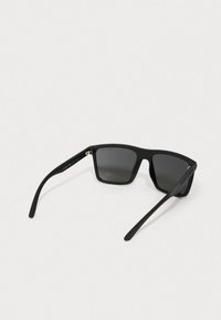 Ochelari de soare negri cu un finisaj mat, cu rame patrate și lentile închise; prezintă o forme elegante ale brațelor și un branding subtil pe partea interioară a brațului.