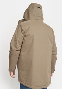 Beige parkajakke med hætte, lange ærmer, knapmanchetter og lige skæring. Glat tekstur og minimal detaljer.