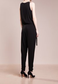 Mono negro de corte holgado, sin mangas, con cinturilla ajustada y bolsillos laterales. Combinado con zapatos de tacón alto negros. Acabado de tela suave.