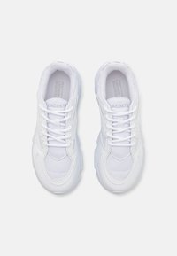 Zapatillas deportivas blancas de material sintético y malla, con punta redonda, collar acolchado, cordones y suela texturizada. Logo de Lacoste en la lengüeta.