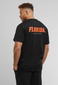 Black cotton t-shirt featuring orange "FLORIDA" text and "UNIVERSITY OF FLORIDA" below, simple crew neck, short sleeves, with a relaxed fit.