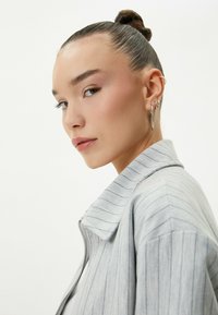 Chaqueta de rayas gris claro con cuello alto y cremallera, que muestra una textura de tela suave y detalles de costura distintivos. La modelo tiene un moño elegante.