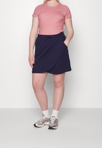 Růžové tričko s krátkým rukávem a kulatým výstřihem, které je kombinováno s tmavě modrou zavinovací sukní se stahovacími šňůrkami a bočními kapsami. Doplněno stříbrnými teniskami.