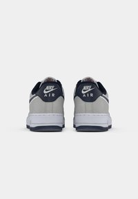 Nike Air tenisice s gornjim dijelom od sive suède, mornarskim naglasima na peti i bijelim međusoleom. Imaju glatku teksturu i teksturirani detalj na peti.
