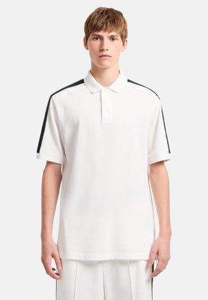 Camiseta polo blanca con cuello clásico, mangas cortas y detalles negros en los hombros. Hecha de tela suave y texturizada con botones.