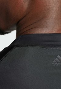 Maglietta sportiva nera con una texture liscia, dettagli delle cuciture e un discreto logo Adidas sul colletto. Vista ravvicinata di lato.