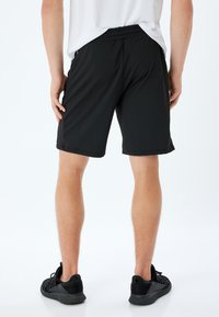 Pantalones cortos deportivos negros con cinturilla elástica, textura suave y paneles laterales de malla transpirable. Ajuste preciso y corte a la altura de la rodilla.