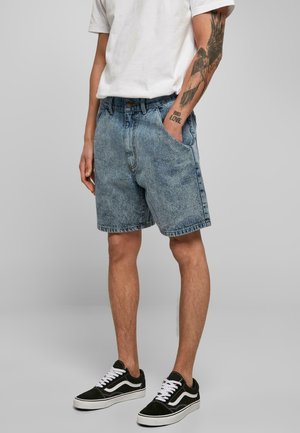 Shorts din denim de culoare albastră deschisă, croială lejeră, cu buzunare vizibile și textură estompată. Asortați cu adidași negri, cu șireturi albe.