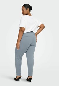 Grå tettsittende bukser med glatt tekstur og elastisk midjebånd, kombinert med en hvit kortermet topp, og brukt med svarte høyhælte sko.