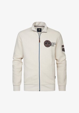 Jachetă crem deschis cu fermoar, cu un model texturat în zigzag, fermoar albastru contrastant și patch cu logo rotund pe piept și accente pe mâneci.