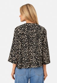Blusa con stampa leopardata in beige e nero, realizzata in tessuto leggero, con una forma ampia e maniche a tre quarti con scollatura rotonda.