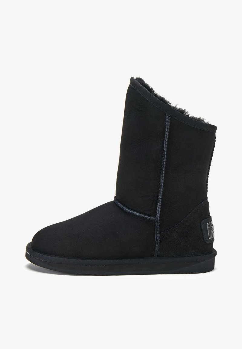 Botín de ante negro con un forro interior suave, puntera redonda y detalles cosidos. Cuenta con una suela de goma y un parche con el logotipo en el costado.