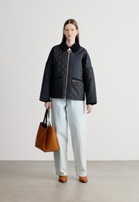 Μαύρο καπιτονέ μπουφάν με ψηλό γιακά, ασημί φερμουάρ και τσέπη. Συνδυασμένο με ανοιχτόχρωμο τζιν παντελόνι και καφετιά τσάντα tote.