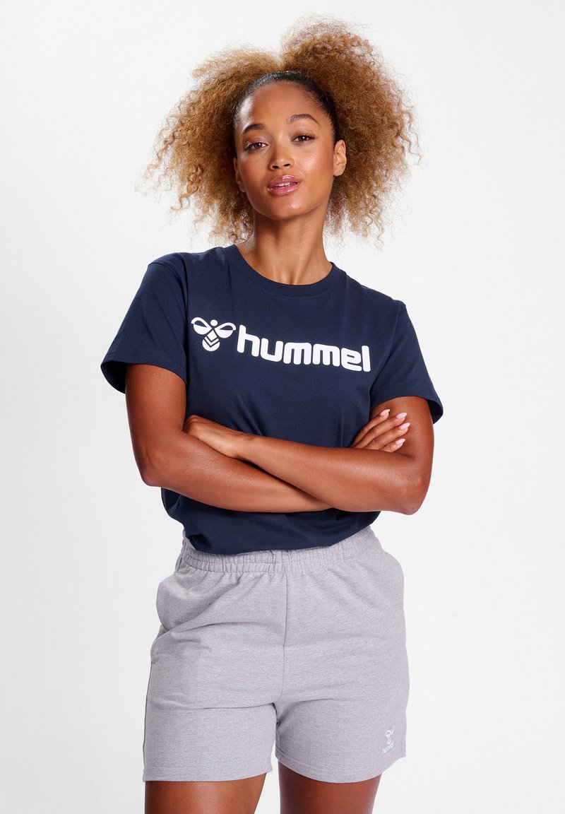 Mörkblå kortärmad T-shirt med vit "hummel"-logotyp, i kombination med ljusgrå shorts. Material i bomull, enkel design, avslappnad passform, elastisk midja.