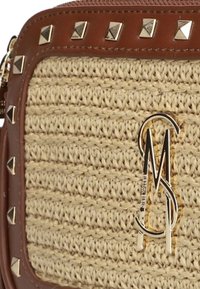 Tan geweven handtas met gouden hardware, piramide-studs langs de rand en een metallic logo detail. Bevat een gestructureerd oppervlak en een rechthoekige vorm.