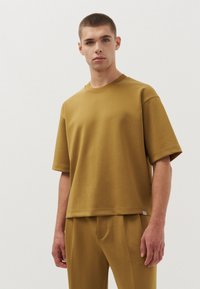 Mosterdgele t-shirt met korte mouwen, met een relaxte pasvorm, ronde halslijn en een soepele textuur, gedragen met bijpassende broek.