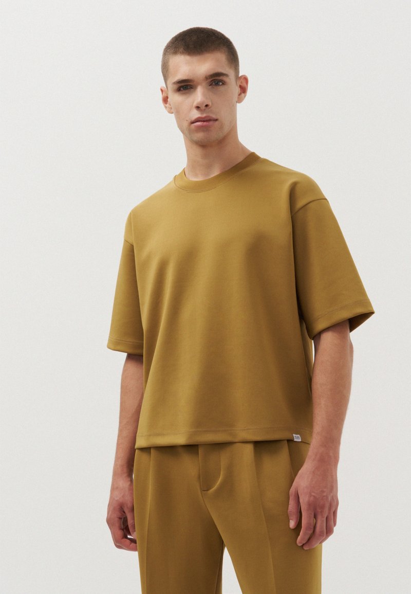 Mosterdgele t-shirt met korte mouwen, met een relaxte pasvorm, ronde halslijn en een soepele textuur, gedragen met bijpassende broek.