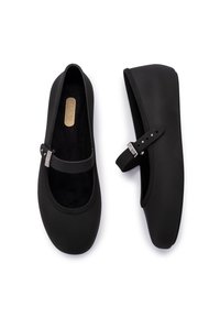 Zapatos planos negros con punta redondeada, correa elástica con detalle de hebilla y textura suave. El interior cuenta con un forro suave.