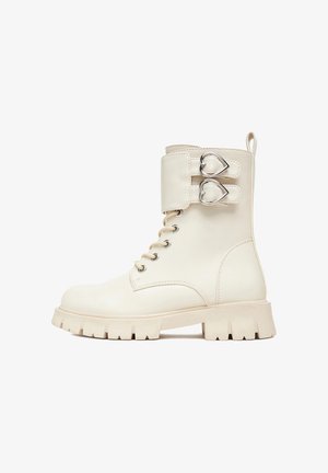 White leather ankle boot with a chunky sole, featuring a side buckle with heart-shaped accents and classic lace-up design.