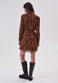 Robe à imprimé léopard orange et noir, à manches longues, avec une taille cintrée et un ourlet court, associée à des bottes noires montantes.