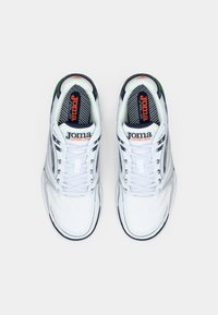 Fehér sportcipők, textúrált bőr felsőrésszel, fűzős dizájnnal, fekete akcentussal és narancssárga logóval a nyelvén. Zöld részlet a saroknál.