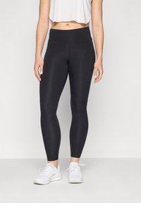 Leggings noirs avec une taille haute, texture lisse et design ajusté. Associer avec des baskets blanches complète le look athlétique.