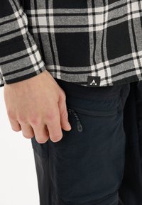 Zwart-witte geruite flanellen blouse met lange mouwen, gecombineerd met zwarte broeken met een ritszak bij de taille.