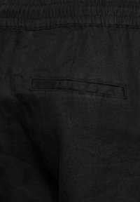 Pantaloni neri in lino con tasca piatta sul retro e vita elasticizzata, che mostrano un tessuto testurizzato e un design semplice.
