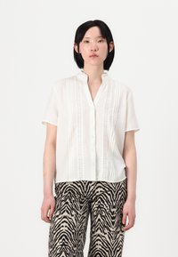 Korte mouwen witte blouse met een lichte kraag, voorzien van verticale textuurstrepen en knoopsluiting, gecombineerd met zwart en beige zebrapatroonbroek.
